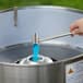 A hand using a Carnival King Floss Bowl Stabilizer Net to pour blue liquid into a metal container.