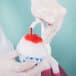 A person in white gloves pouring Carnival King Strawberry Snow Cone Syrup onto a snow cone.