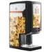 A black Carnival King peristaltic cheese sauce dispenser on a counter with a picture of nachos.