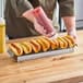 A man using a Carnival King stainless steel hot dog preparation tray to put ketchup and mustard on hot dogs.