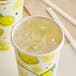 A clear plastic Carnival King cold cup lid with a straw slot over a lemonade cup with lemons on it.