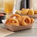 A Carnival King paper food tray filled with fried onion rings and a cup of ketchup on a table.