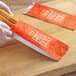 A person placing a hot dog in a red and white logoed paper bag.