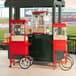 A red Carnival King popcorn cart with a red umbrella attached to it.