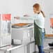 A woman standing in front of a Carnival King countertop fryer in a kitchen.