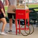 A couple standing next to a Carnival King popcorn cart filled with popcorn.