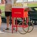 A man standing next to a red cart with a Carnival King popcorn machine.