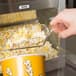 A hand using a Carnival King clear plastic utility scoop to serve popcorn.