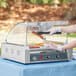 A person using a Carnival King glass sneeze guard to prepare hot dogs on a hot dog roller grill.