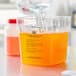 A person pouring orange liquid from a measuring cup into a clear container.