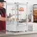 A man in a red apron using a Carnival King countertop pizza display warmer to serve pizza.