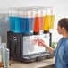 A woman pouring liquid into a Carnival King refrigerated beverage dispenser.