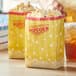 Two yellow Carnival King popcorn bags on a table with a drink.